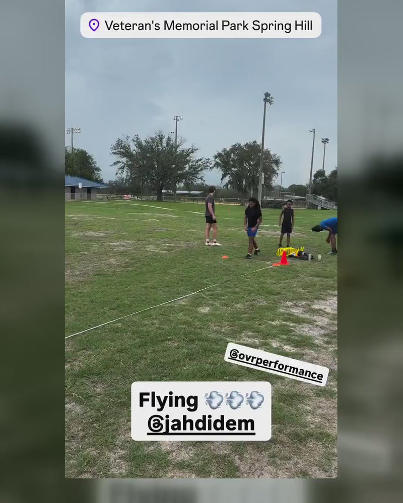 An athlete runs a flying sprint past timing gates on a field marked out with an EZCones measuring tape and marker.
