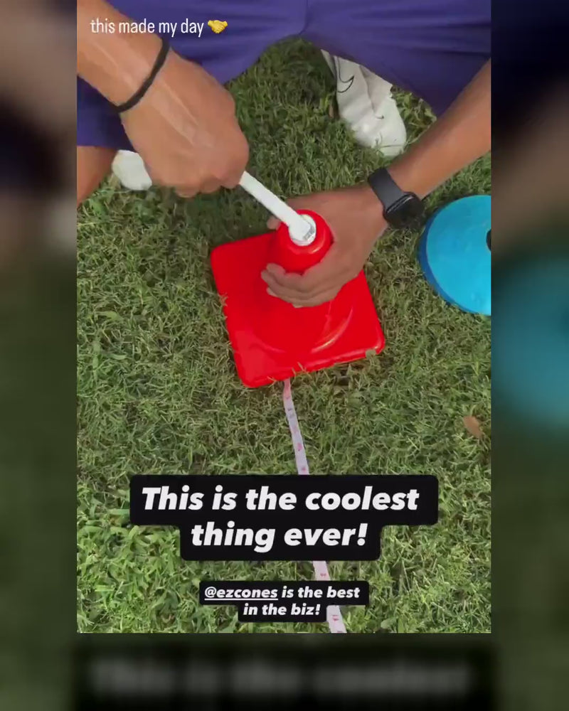 A coach kneels on the grass and pulls the measuring tape out of an orange EZCone, then follows the tape down the practice field.